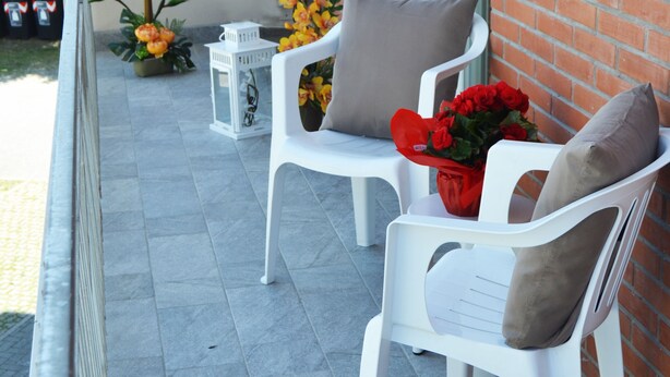 A balcony with two white plastic chairs, a small table, and a bouquet of red roses. - Apartment 100 meters from the beach (Gatteo A Mare)