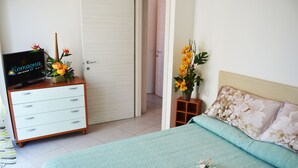 A bedroom with a bed, a dresser, a TV, and a door. - Apartment 100 meters from the beach (Gatteo A Mare)