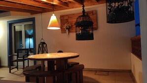 A dining area with a round wooden table and chairs, a hanging pendant light, and a wall-mounted birdcage. - CASA DAMÉLIA POLO2-House near Óbidos in the slope of recycling décor (Vau Óbidos)