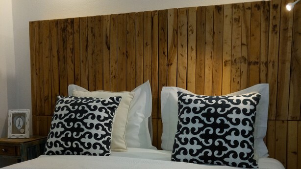 A neatly made bed with white linens and patterned pillows, a wooden headboard, and a wall clock. - CASA DAMÉLIA POLO2-House near Óbidos in the slope of recycling décor (Vau Óbidos)
