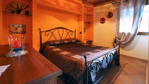Une chambre à coucher avec un lit, une table de chevet en bois, un vase en verre avec une bougie et une fenêtre avec des rideaux.