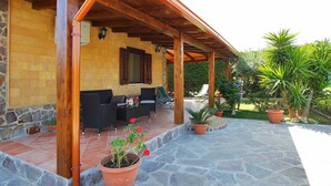 Un espace extérieur aménagé avec des meubles en osier, un sol en pierre et des plantes en pot, le tout abrité.
