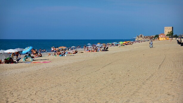 Une vaste plage de sable, parsemée de parasols et fréquentée par de nombreuses personnes.