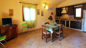 Un coin repas avec une table dressée pour quatre personnes, un téléviseur posé sur un meuble et une cuisine en arrière-plan.