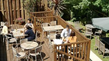 An outdoor patio area with wooden deck, metal and wooden chairs, and tables.