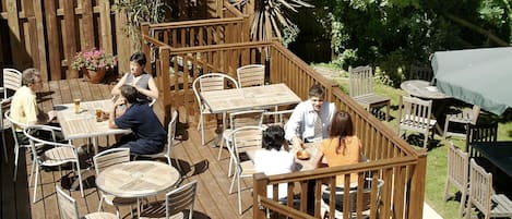Un área de patio al aire libre con cubierta de madera, sillas de metal y madera, y mesas.