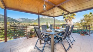 An outdoor patio with a wooden ceiling, a table with chairs, and a view of mountains. - VILVAL Finca for 4 with pool in Moscari (Moscari)