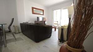 Un salón con sofá, sillón, radiador, lámpara y un jarrón con ramas.