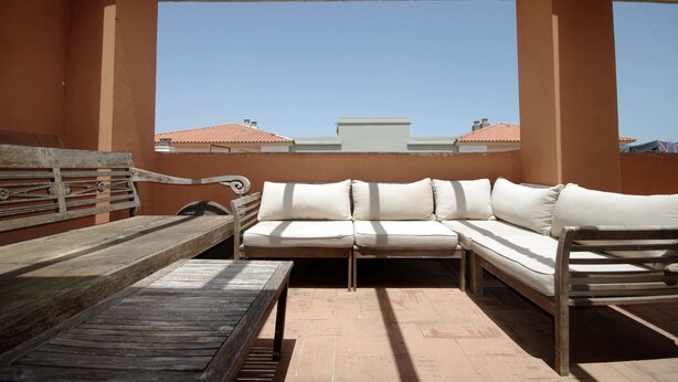 Una terraza en la azotea con un sofá blanco, un banco de madera y una mesa.
