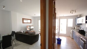 Una cocina moderna con electrodomésticos de acero inoxidable, un comedor con mesa y sillas de vidrio, y una sala de estar con sofá y televisor.