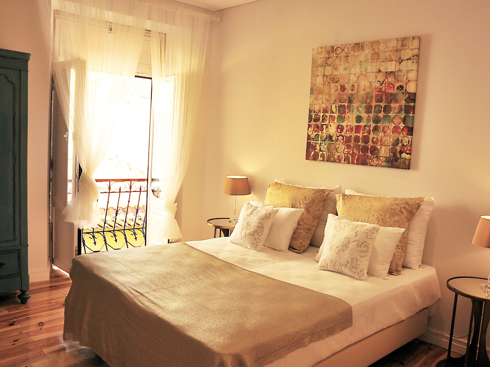 A bedroom with a bed, two bedside tables, a window with curtains, and a wall-mounted artwork.