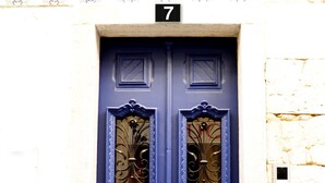 Eine blaue Doppeltür mit aufwendiger Metallverzierung, darüber die Zahl 7 und ein kleines Fenster zur Rechten.