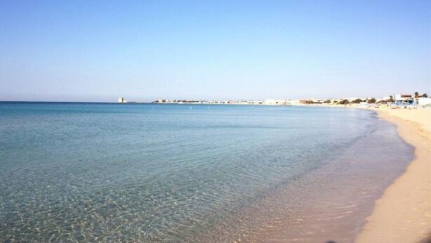 Una playa con agua cristalina, una orilla arenosa y edificios a lo lejos.