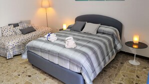 Een keurig opgemaakt slaapkamer met een bed, een bank en een nachtkastje met een lamp.