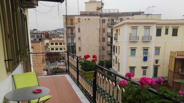 Een balkon met twee groene stoelen, een kleine tafel en potplanten met rode bloemen.