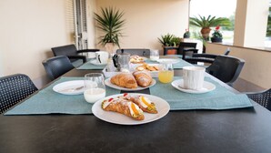 A dining table set with plates, glasses, and food items, surrounded by chairs and potted plants. - Ninfa Charming Accomodation in the Eastern Coast (Floridia)