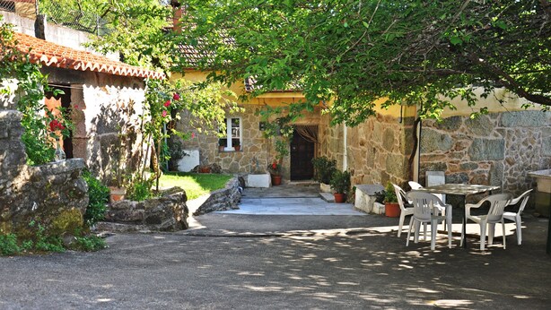 Ein Gebäude aus Stein mit Ziegeldach, einem gepflasterten Innenhof und einem Tisch mit Stühlen.