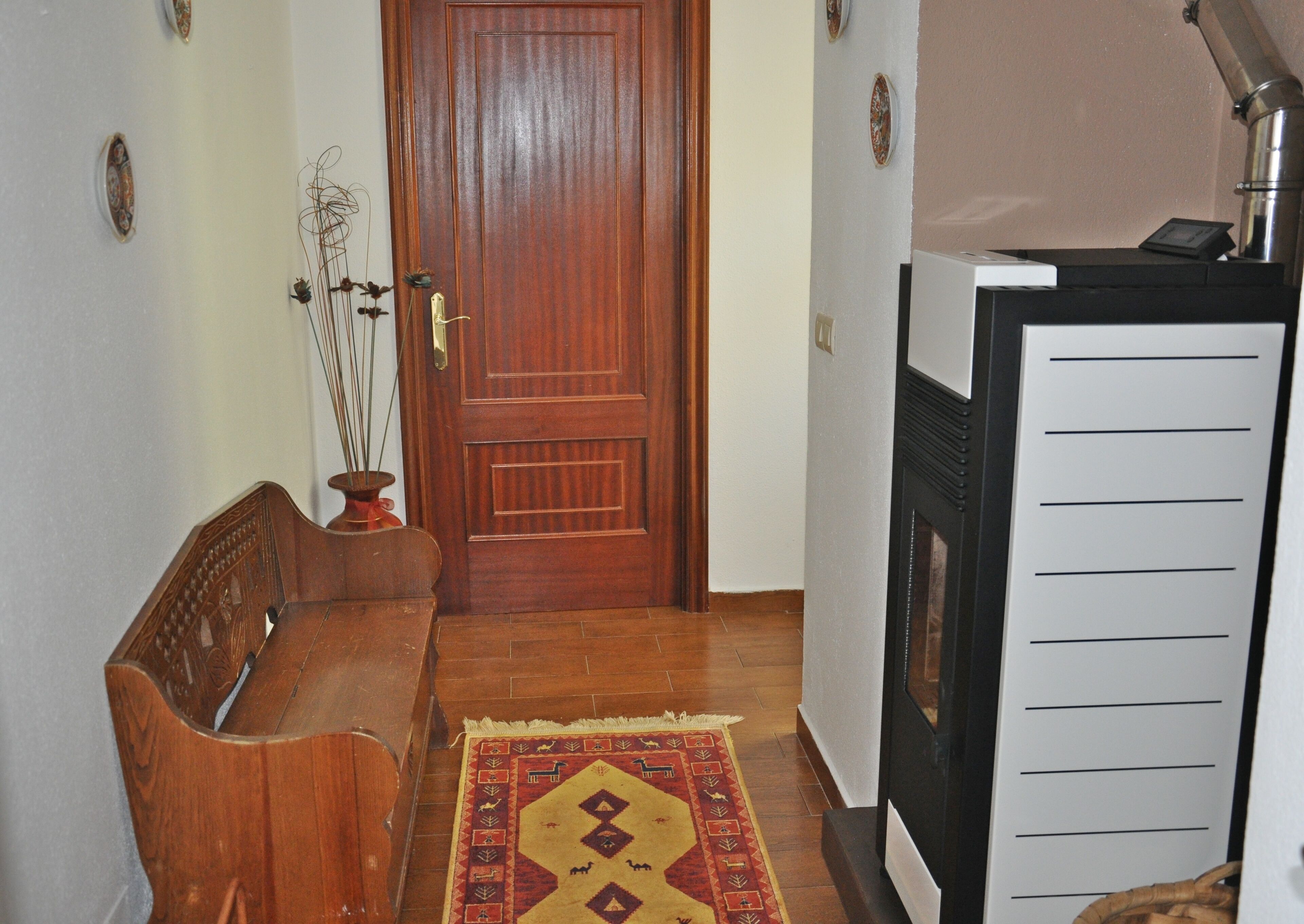 A hallway with a wooden bench, a patterned rug, a door, and a white appliance with a control panel.