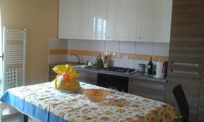 A kitchen with white cabinets, a gas stove, and a table with a fruit-patterned tablecloth. - Lucca apartment good price close to station & center (Lucca)