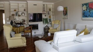 A living room with a fireplace, white sofas, a yellow armchair, and a TV.