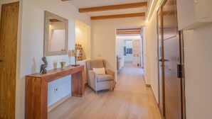 Un hall d’entrée spacieux avec un plancher en bois, une console en bois surmontée d’un miroir, un fauteuil beige et une porte donnant sur une autre pièce.