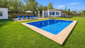 Une piscine aux carreaux bleus, entourée d’une pelouse bien entretenue et d’un bâtiment blanc aux volets bleus.