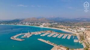 Vue aérienne d’une marina côtière où sont amarrés des bateaux, entourée d’une ville et avec des montagnes en arrière-plan.