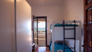 Ein kleines Zimmer mit Etagenbett, einem Tisch und Meerblick durch eine offene Tür.
