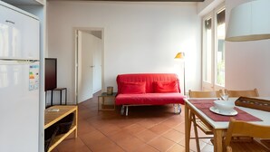 Ein gemütlicher Wohnbereich mit einem roten Sofa, einem Esstisch mit Stühlen, einem Fernseher und einer Lampe.