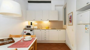 Eine kleine Küche mit weißen Schränken, einer Mikrowelle, einem Toaster und einem Spülbecken. Ein Esstisch mit Stühlen und einer roten Tischdecke ist ebenfalls vorhanden.