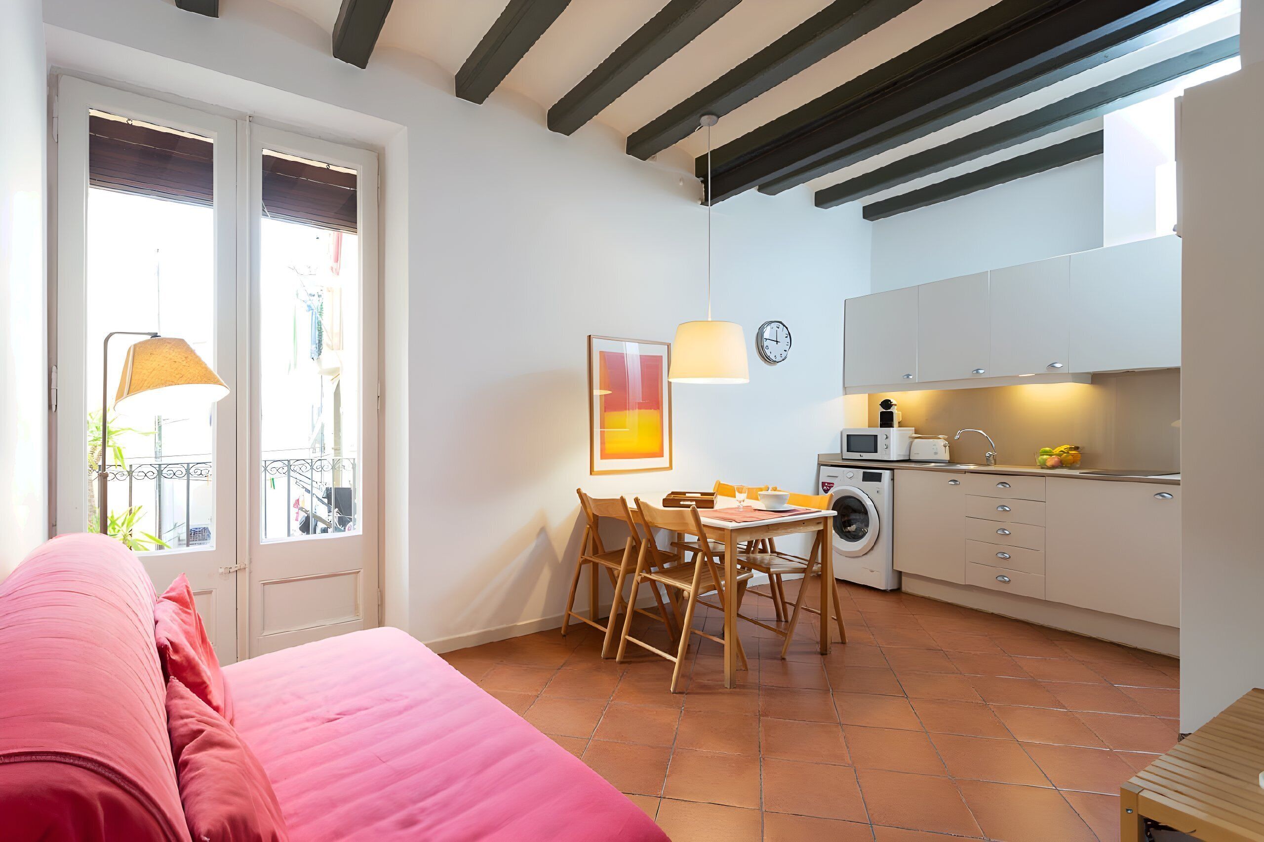 Un espace de vie compact comprenant un lit, un coin repas avec des chaises, un lave-linge et une kitchenette.
