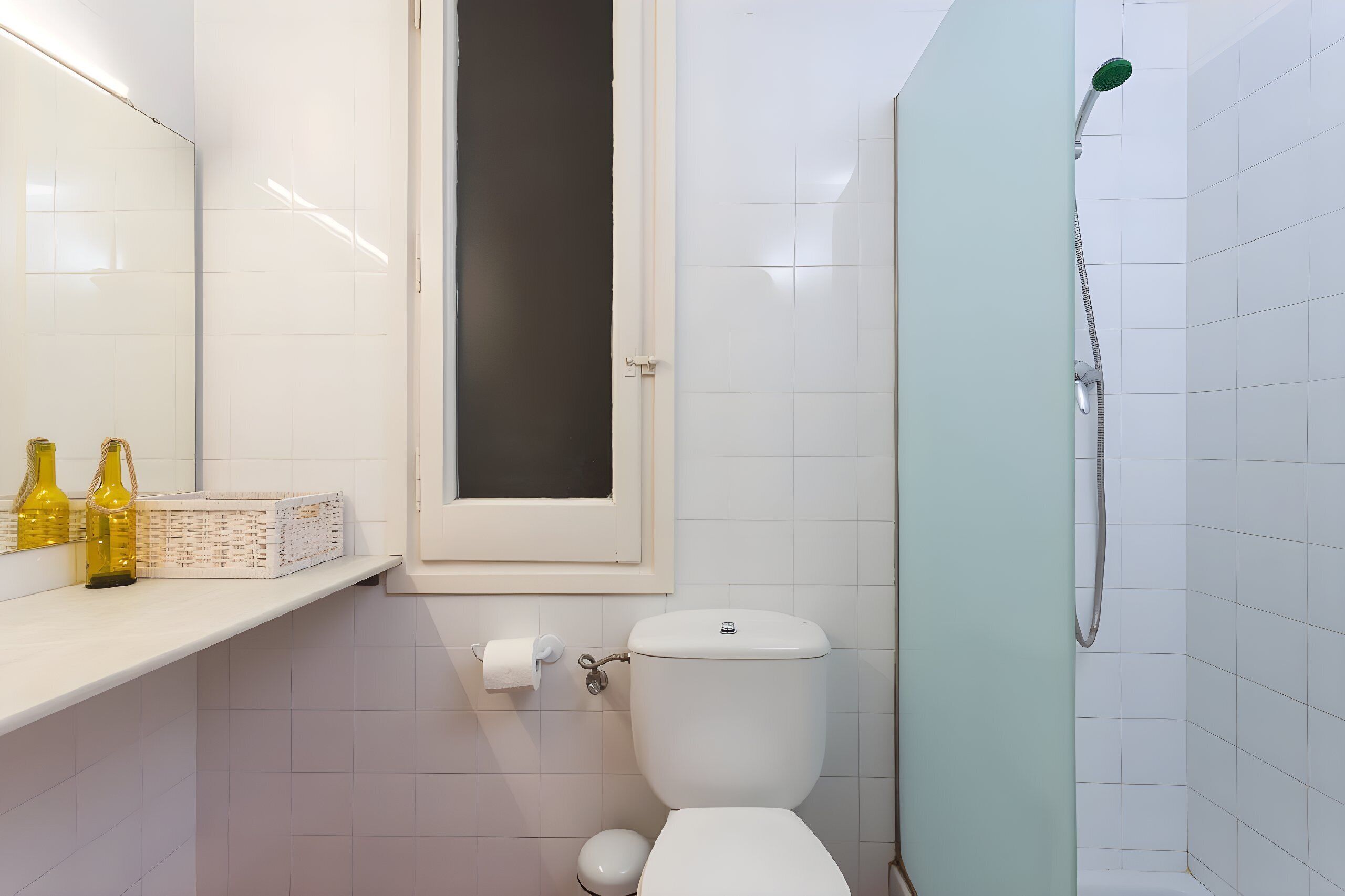 A bathroom with a toilet, a shower, and a shelf with bottles.