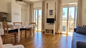 Una sala de estar con un sofá azul, una mesa de comedor de madera, sillas y un televisor.