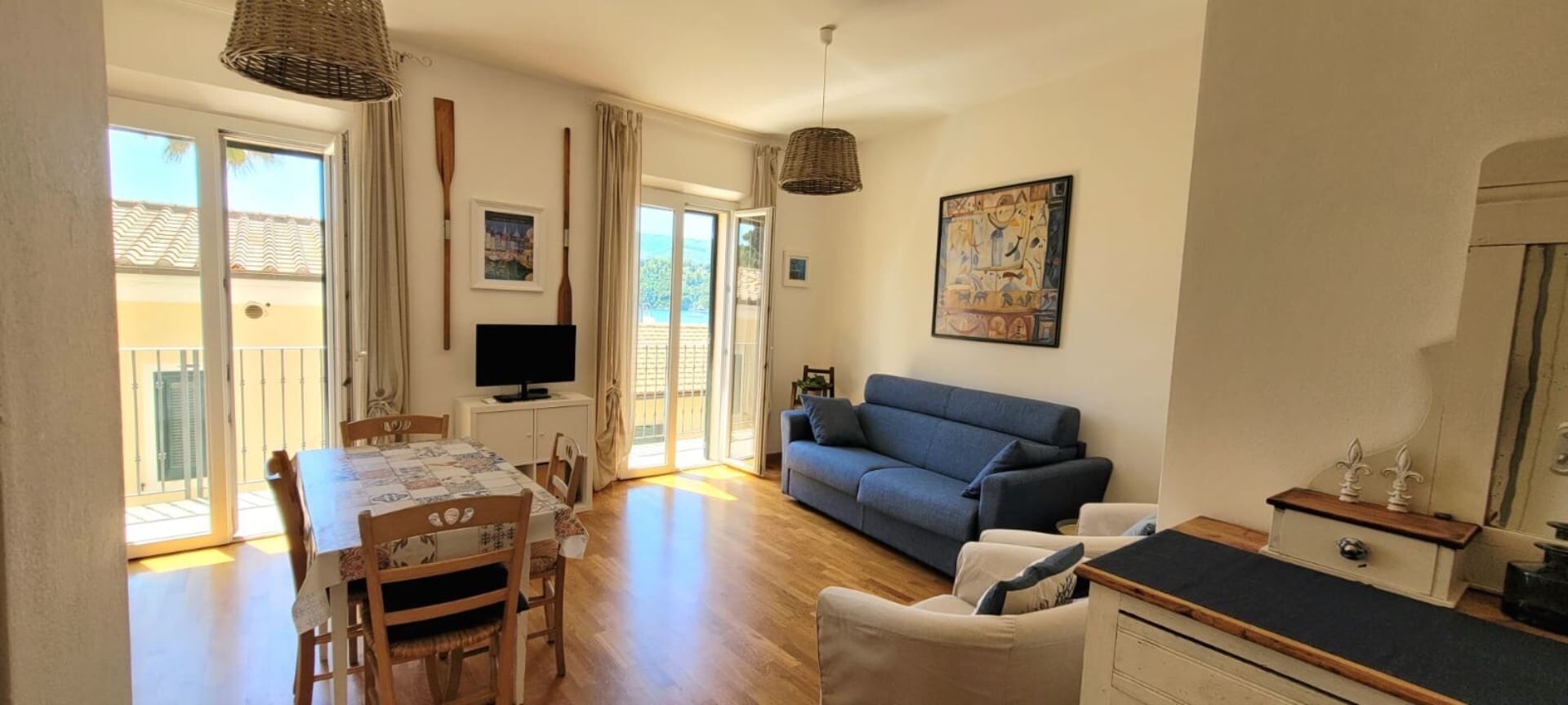 A living room with a sofa, a dining table with chairs, a TV, and a painting on the wall.