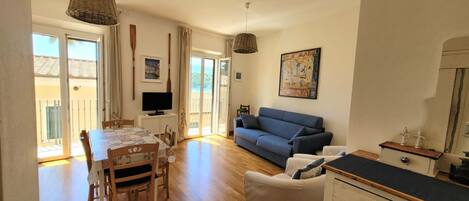 A living room with a sofa, a dining table with chairs, a TV, and a painting on the wall.