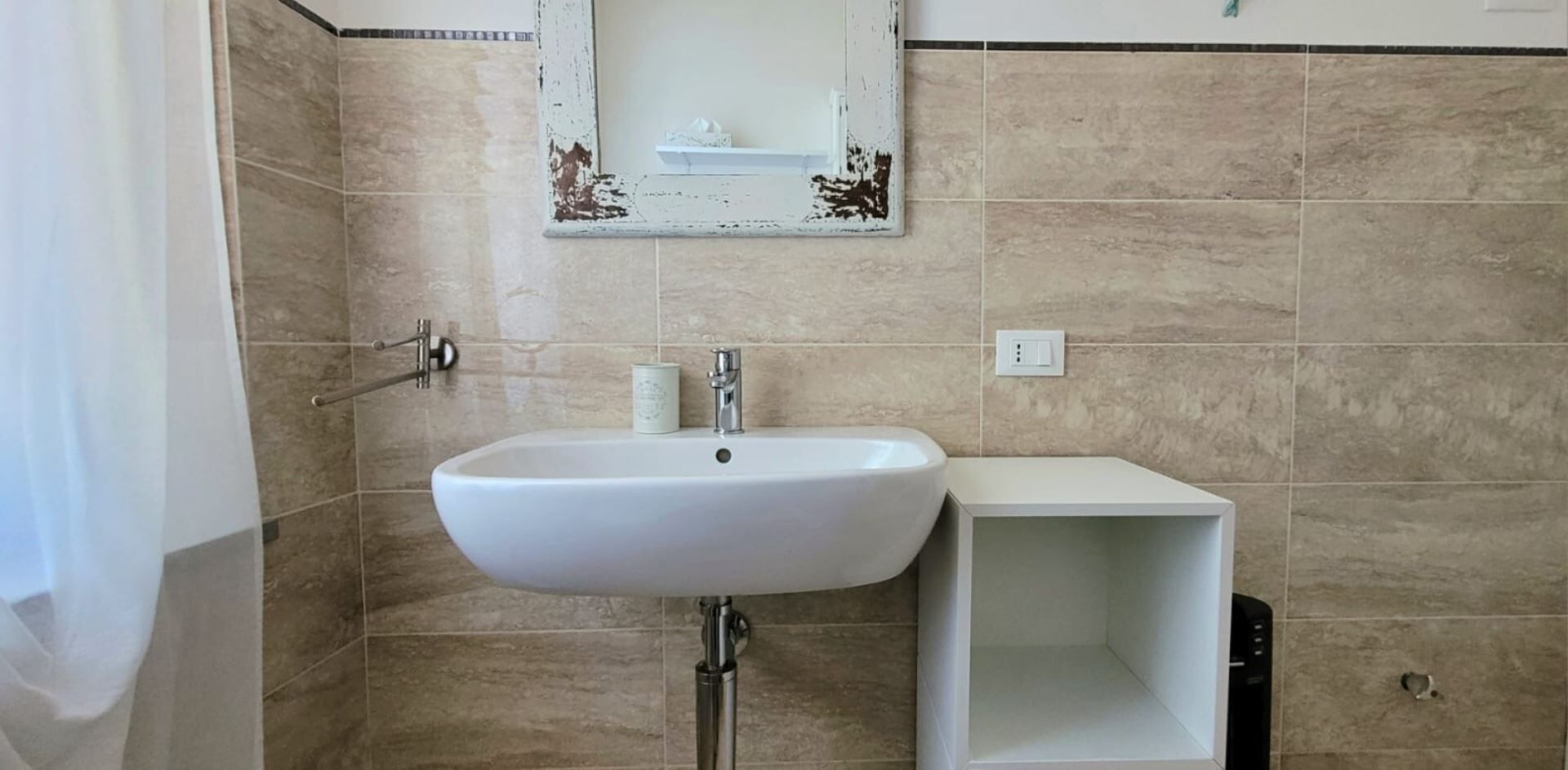Une salle de bain avec un lavabo blanc, un miroir et un mur recouvert de carreaux.