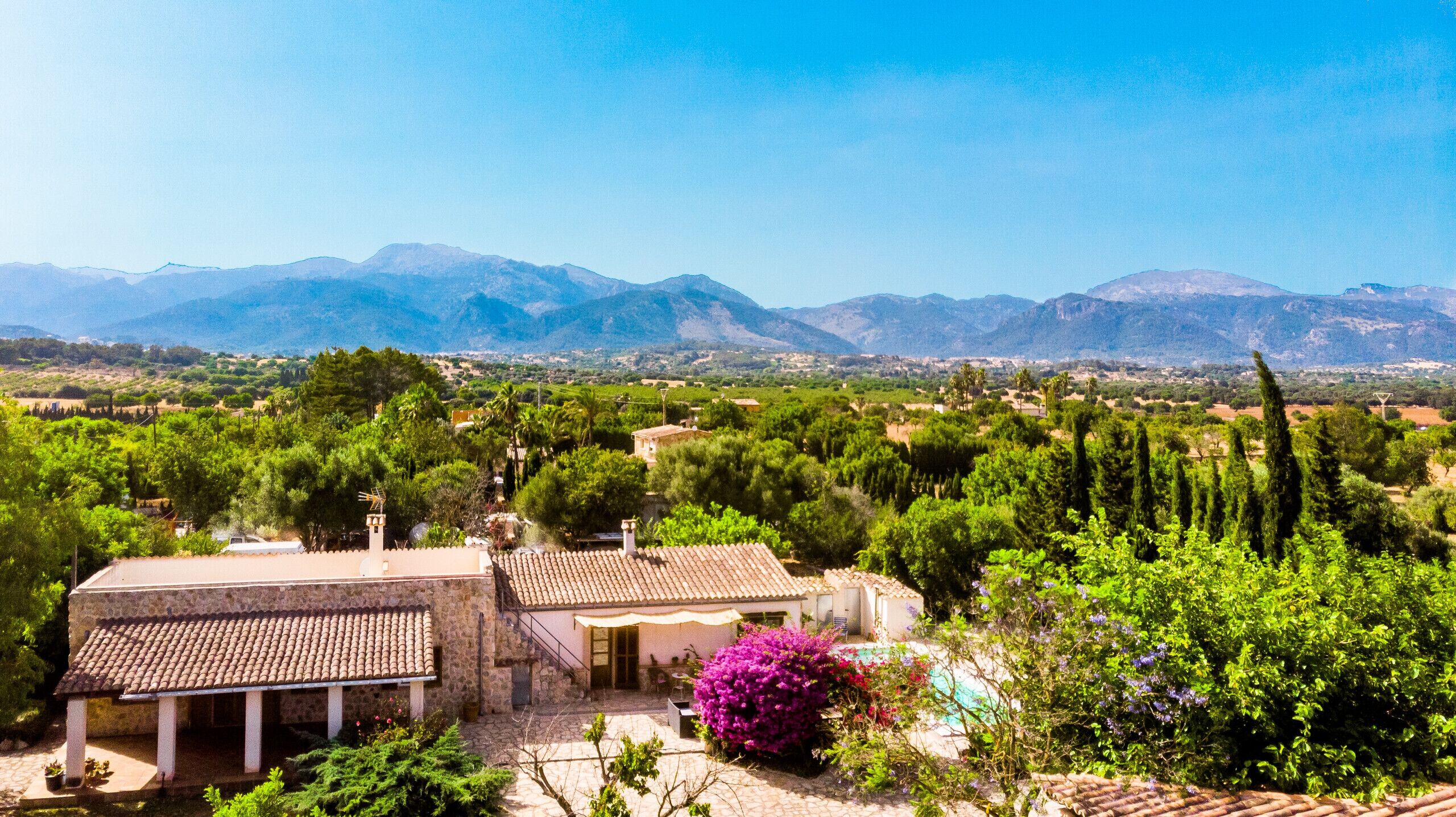 A villa with a tiled roof, surrounded by lush greenery and a view of distant mountains.