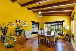 A dining area with a wooden table and chairs, a hanging light fixture, and a window with blinds. - PORXET In the heart of the island, an oasis of peace with a swimming pool for 6 (Inca)
