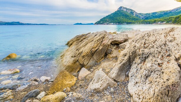 Un littoral rocheux, avec une eau claire et des montagnes qui se dessinent à l’horizon.