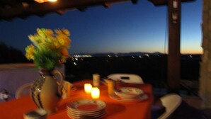 Ein Essbereich im Freien mit einem Tisch für zwei Personen, einer Blumenvase und Blick auf die Stadt bei Dämmerung.