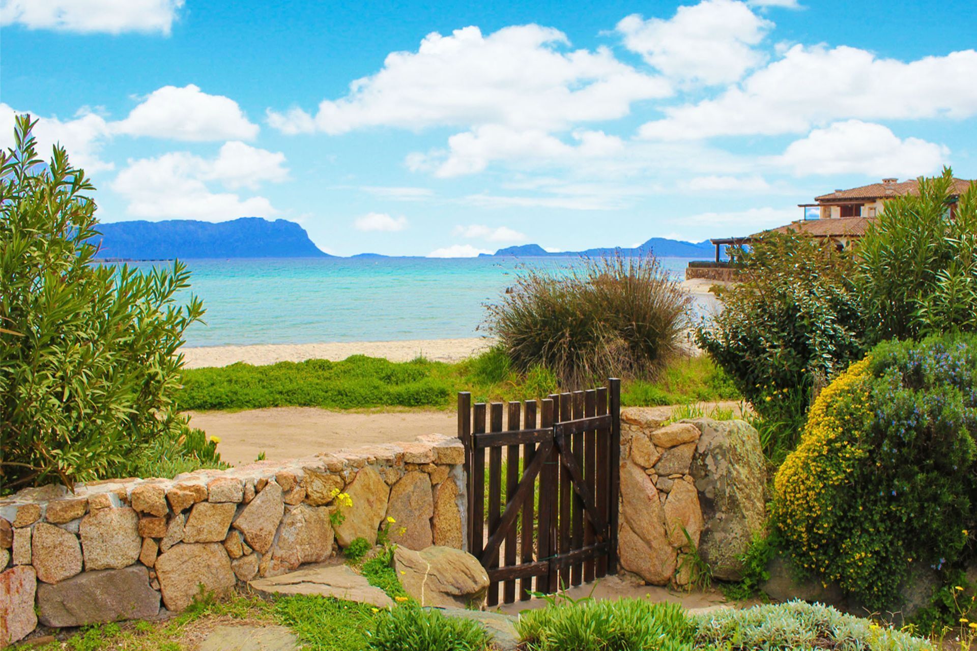 A coastal property with a stone wall and wooden gate leading to a beach.