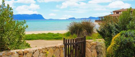 A coastal property with a stone wall and wooden gate leading to a beach.