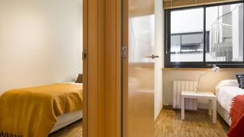 A modern bedroom with a wooden floor, a bed with a yellow blanket, a bedside table with a lamp, and a window with a view of the outside.