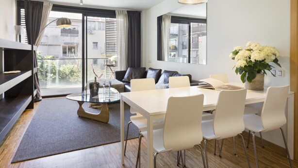 A modern living room with a dining area, large windows, and a view of the city.