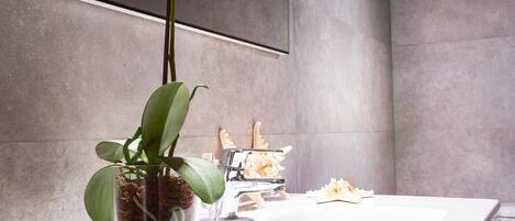 A bathroom with a white sink, a potted orchid, and a decorative coral piece.