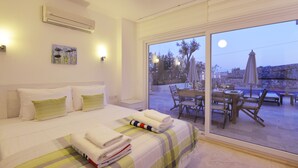 A hotel room with a bed, a painting, an air conditioner, and a view of the outdoor patio area. - Elmas Apt - Luxury 3BR with Large Private Pool & Garden. 10 min Walk to Town! (Kalkan)