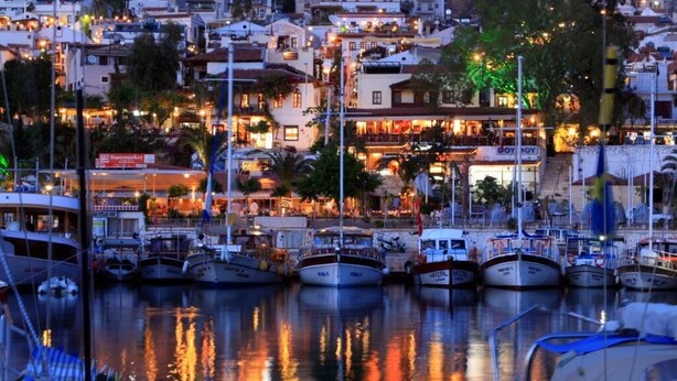 A marina with boats docked, surrounded by buildings with illuminated signs and lights. - Elmas Apt - Luxury 3BR with Large Private Pool & Garden. 10 min Walk to Town! (Kalkan)