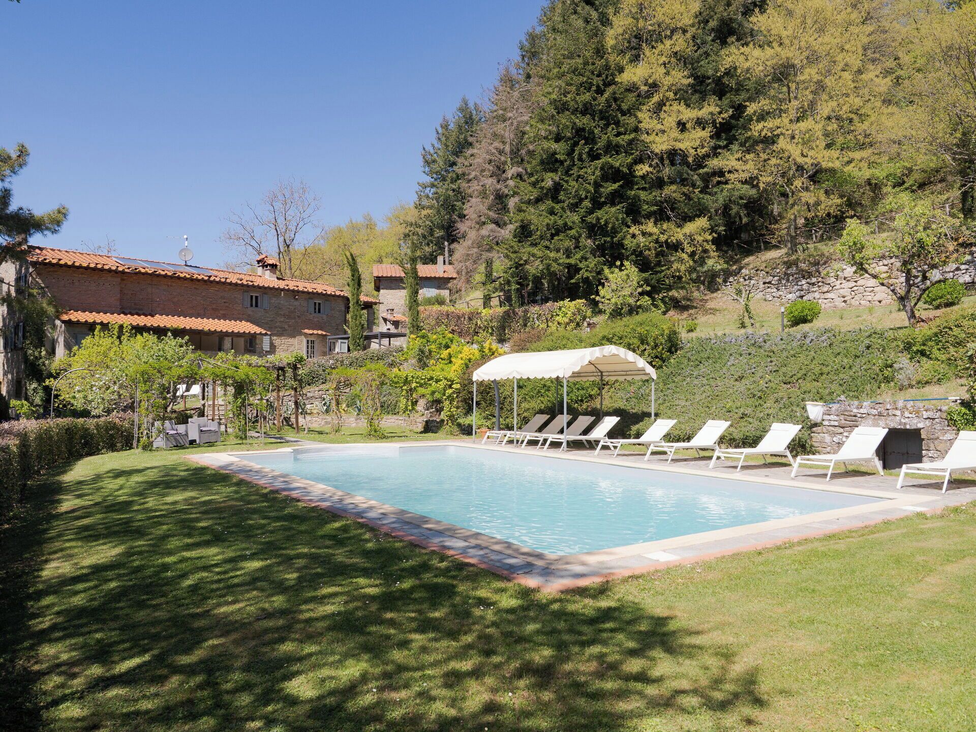 A swimming pool with lounge chairs and a canopy, surrounded by a well-maintained lawn and a stone wall.