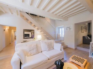 Un'ampia zona giorno con un divano bianco, una scala e una scacchiera su un tavolo in legno.