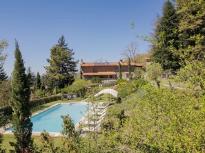 Una piscina con lettini, immersa nel verde e affiancata da un edificio con tetto in tegole.